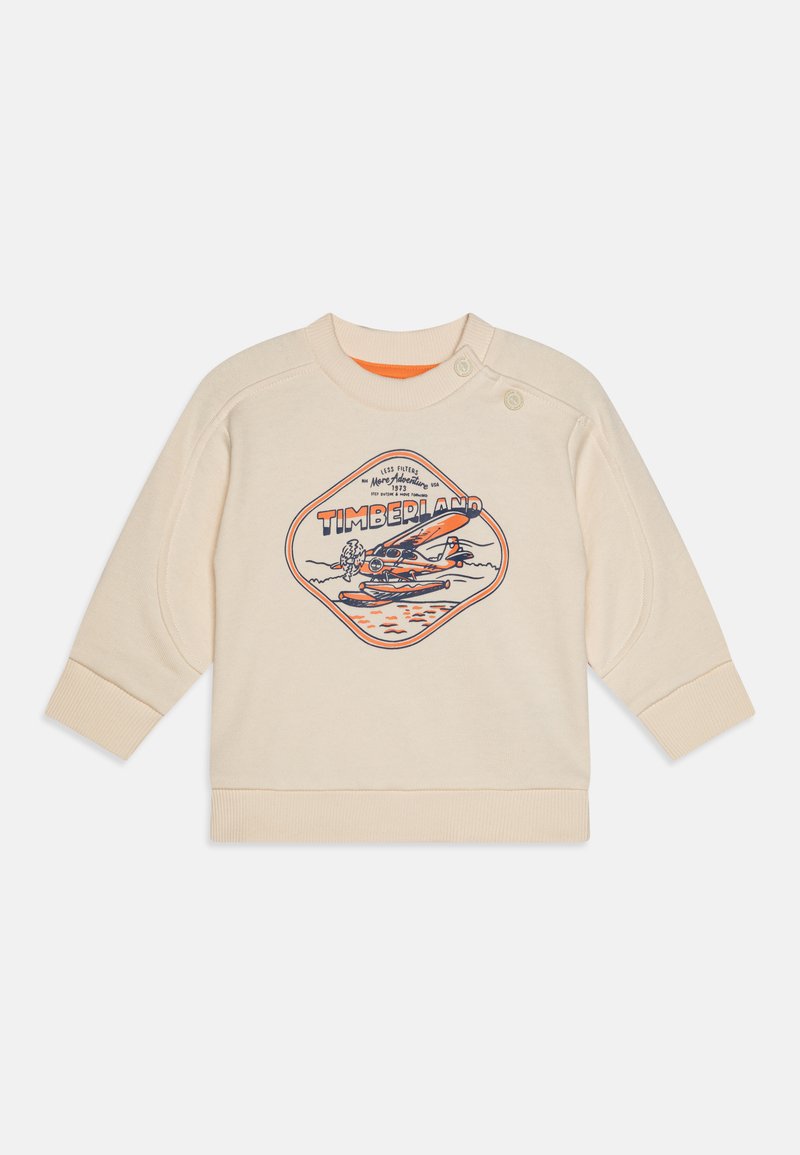 Krämfärgad sweatshirt med rund halsringning, med ett grafiskt tryck av ett flygplan och "TIMBERLAND." Inkluderar knappdetaljer på axeln.