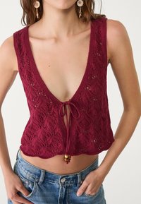 Top en tricot bordeaux avec un décolleté en V profond, doté d'une fermeture à nouer et d'un ourlet festonné. Le tissu présente un motif texturé en dentelle.