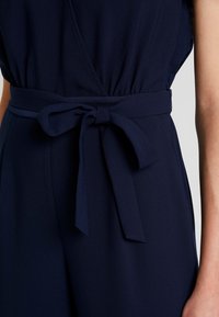 Vestido azul marino con un cinturón de tela atado en forma de lazo en la cintura, mostrando parte del brazo y torso de una persona.