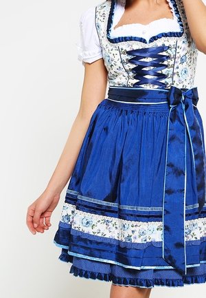 Vue recadrée d’une personne portant un dirndl bleu avec un corsage à motif floral, un laçage sur le devant, un chemisier blanc et une jupe ample.