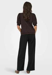 Brown pullover with puff sleeves and ribbed cuffs, paired with high-waisted black wide-leg pants and brown textured shoes.