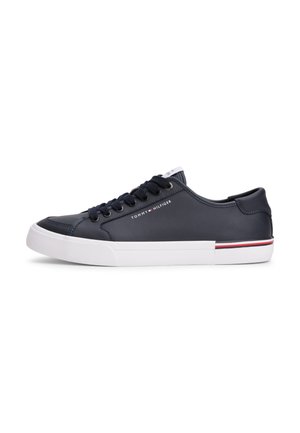 Baskets basses bleu marine avec semelle blanche, lacets noirs, petit logo Tommy Hilfiger sur le côté et bande rouge et blanche sur le bord de la semelle.