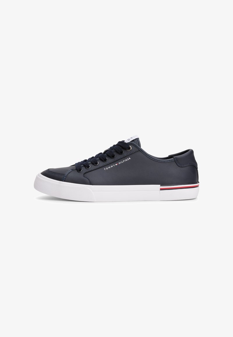 Baskets basses bleu marine avec semelle blanche, lacets noirs, petit logo Tommy Hilfiger sur le côté et bande rouge et blanche sur le bord de la semelle.