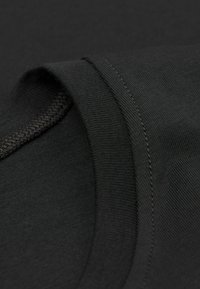 Czarna bawełniana koszulka z gładką teksturą, okrągłym dekoltem i widocznymi detalami szwów. Zbliżenie na materiał i wzór kołnierza.