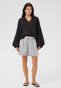 Blusa nera leggera con scollo a V e maniche morbide, abbinata a una gonna in denim grigia e infradito nere.