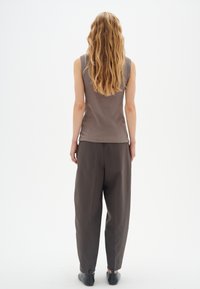 Šedý bezrukávový top kombinovaný s tmavě šedými volnými kalhotami; modelka má dlouhé, vlnité vlasy a nosí černé ploché boty. Jednoduchý design.