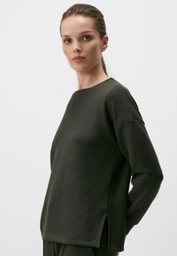 Donkergroen sweatshirt van zacht materiaal, met een relaxte pasvorm, ronde halslijn en zijsplitten aan de zoom voor extra detail.