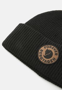 Czarna, prążkowana czapka beanie z podwiniętym mankietem, z okrągłą brązową łatką logo przedstawiającą głowę lisa oraz napisem "Forever Bergtagen."