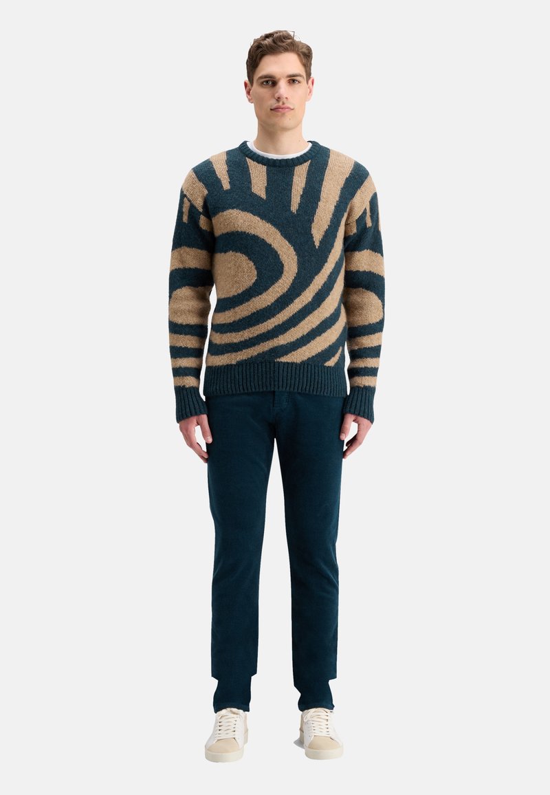 Strickpullover in Dunkelblau und Beige mit abstraktem Spiralmuster. Lange Ärmel, gerippte Bündchen und Saum. Kombiniert mit dunklen Hosen und Sneakers.