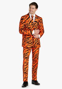 Completo arancione brillante con strisce nere a forma di tigre, dotato di giacca monopetto e pantaloni abbinati. Scarpe nere completano l'outfit.