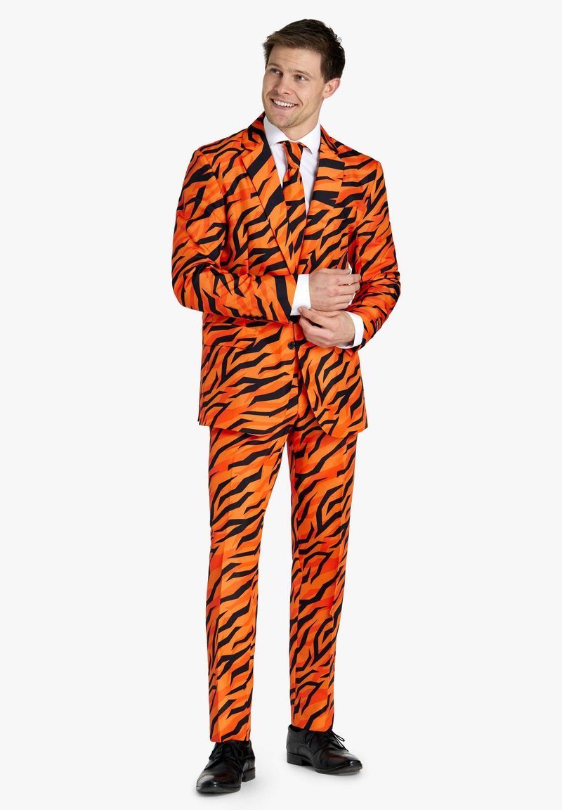 Completo arancione brillante con strisce nere a forma di tigre, dotato di giacca monopetto e pantaloni abbinati. Scarpe nere completano l'outfit.