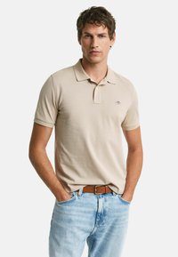 Polo shirt in cotone beige con maniche corte, colletto e un piccolo logo. Abbinato a jeans in denim blu chiaro e una cintura marrone.