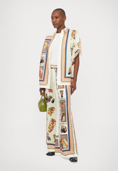 Compleu format din două piese, care include o cămașă deschisă la culoare cu nasturi și pantaloni largi cu modele de fructe și vase în culori vibrante, plus o poșetă verde.