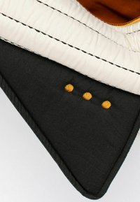 Tessuto nero con fodera color crema e cuciture arancioni. Ricami dorati formano tre punti sul lato nero, evidenziando la texture e il contrasto di colore.