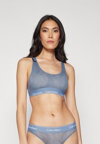 Soft blue bralette with a textured pattern, wide straps, and elastic band featuring the Calvin Klein logo. Matching underwear included.