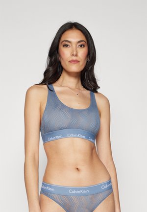 Meka plava braletica s teksturiranim uzorkom, širokim naramenicama i elastičnom trakom s logotipom Calvin Klein. Uključeni su usklađeni gaćice.