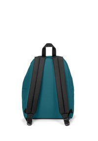 Mochila de tela color azul verdoso con correas negras, forma redondeada, asa superior y sin herrajes visibles ni patrones en la superficie.