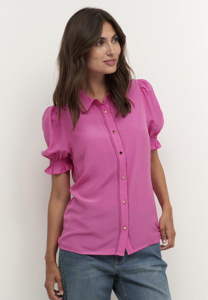 Fuchsia blouse with a collared neckline, button front, and puffed short sleeves. Features elastic cuffs and decorative stitching. Casual fit.