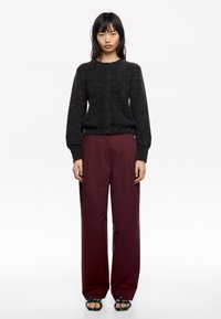 Suéter de punto gris oscuro con cuello redondo y cierre de botón, combinado con pantalones anchos burdeos y sandalias negras con detalles verdes.