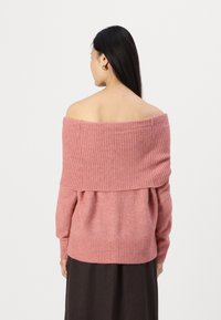 Rožinė off-the-shoulder megzta palaidinė su įrimuota tekstūra, ilgomis rankovėmis ir plačiu iškirpimu. Medžiaga atrodo švelni ir megzta.