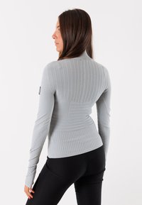 Maglione grigio a maniche lunghe con collo alto, caratterizzato da pannelli testurizzati e una silhouette aderente. Leggings neri completano l'outfit.