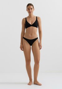 Črni bikini komplet s trikotnim zgornjim delom braletke z nastavljivimi naramnicami in ujemajočimi se nizko postavljenimi hlačkami. Gladek material z minimalističnim dizajnom.