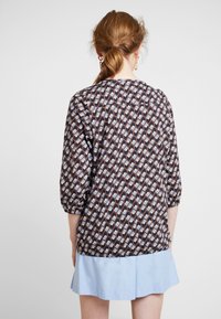 Blusa marrone a fantasia con maniche a tre quarti, forme geometriche e orlo leggermente arricciato in basso. Sottogonna blu chiaro.