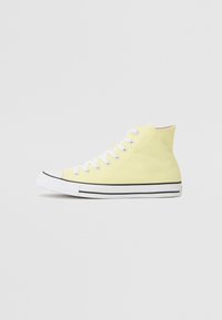 Hochschnitt-Sneaker aus weichem gelben Canvas mit weißen Schnürsenkeln, Kautschukzehenkappe und schwarzen Streifendetails entlang der Sohle. Minimalistische Markenkennzeichnung.