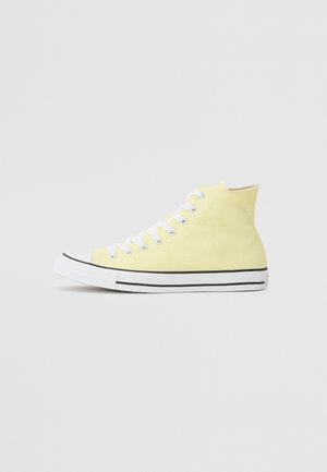 Hochschnitt-Sneaker aus weichem gelben Canvas mit weißen Schnürsenkeln, Kautschukzehenkappe und schwarzen Streifendetails entlang der Sohle. Minimalistische Markenkennzeichnung.