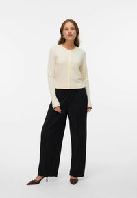 Ljusbeige kofta med knappar, figursydd design och långa ärmar. Matchad med svarta, ribbade vida byxor och spetsiga bruna klackar.