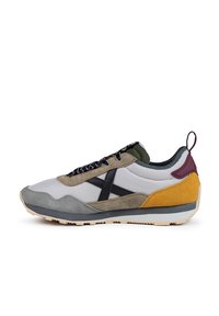 Zapatilla deportiva multicolor con una mezcla de materiales en gris, negro, verde y amarillo. Presenta un upper texturizado y una suela de goma.