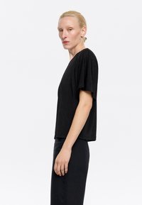 Top nero a maniche corte con vestibilità morbida e texture soffice, caratterizzato da un profondo scollo a V e dettagli minimi, abbinato a pantaloni neri.