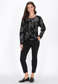 Maglione nero con motivo floreale e accenti argentati, abbinato a pantaloni neri slim-fit e mocassini neri. Tessuto liscio, scollatura rotonda.