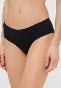 Boxer de algodón negro con un borde festoneado, textura suave y un diseño clásico. Se ajusta cómodamente con una subida media.