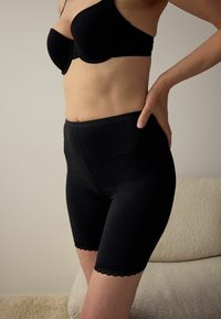 Fekete, magas derekú rövidnadrág puha anyagból, sima felülettel és finom, hullámos csipke díszítéssel a szegélyén.