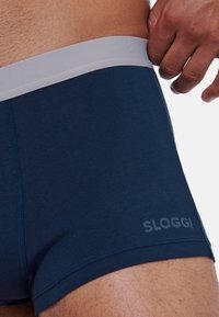 Boxer shorts Sloggi di colore blu navy con elastico grigio chiaro. Materiale morbido e elastico con cuciture rinforzate e dettagli logo sul lato.