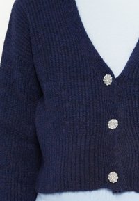 Námořnický pletený kardigan s designem ve tvaru V, který má tři ozdobné stříbrné knoflíky a texturovaný žebrovaný vzor na látce.