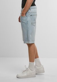 Lyseblå denimshorts med en afslappet pasform, der har sidelommer, omdrejede kanter og kontraststrik. Båret med hvide sneakers og sokker.