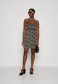 Rochie cu un model alb-negru, cu talie ajustată, bretele subțiri și fustă evazată. Asortată cu pantofi cu toc bloc negri și ochelari de soare.