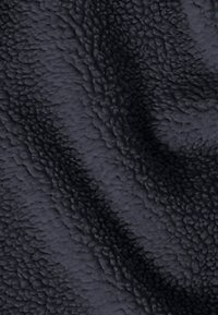 Zwart, gestructureerde stof die lijkt op fleece met een zachte, pluisachtige oppervlakte en met golven en plooien, wat een dynamisch visueel patroon creëert.