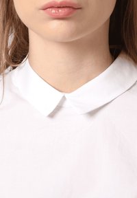 Camisa blanca de cuello con una textura de tela suave, que presenta un cuello plano clásico y un cierre de botones en el cuello.