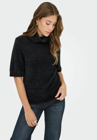 Suéter negro de manga corta y cuello alto con una textura suave y peluda, y dobladillo acanalado; combinado con jeans de mezclilla oscuros.