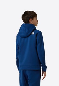 Kék kapucnis pulóver kapucnival, puha anyagból készült. A The North Face fehér logója található a felső hátrészen, bordázott mandzsettákkal és szegéllyel.