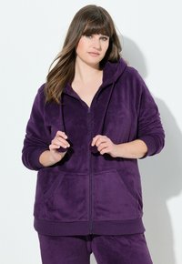 Haut à capuche zippé en polaire violet avec deux poches avant, capuche avec cordon de serrage et poignets côtelés. Texture douce avec une coupe décontractée.
