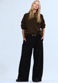 Brun oversized strikket sweater med op rullede ærmer, kombineret med sort højtaljede bukser med vide ben og sort fodtøj.