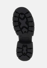 Suela de zapato de goma negra con una superficie texturizada, que presenta un patrón de tacos para agarre y un logo de marca en relieve.