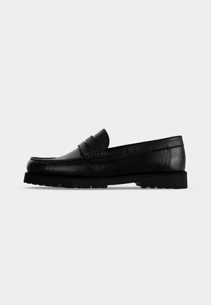 Chaussure mocassin penny en cuir noir avec dessus texturé et semelle épaisse à relief, présentée de profil sur un fond clair uni.