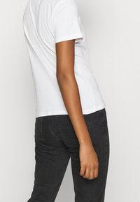 White cotton t-shirt with short sleeves and a round neckline, paired with dark denim jeans; the fabric appears smooth and untextured.