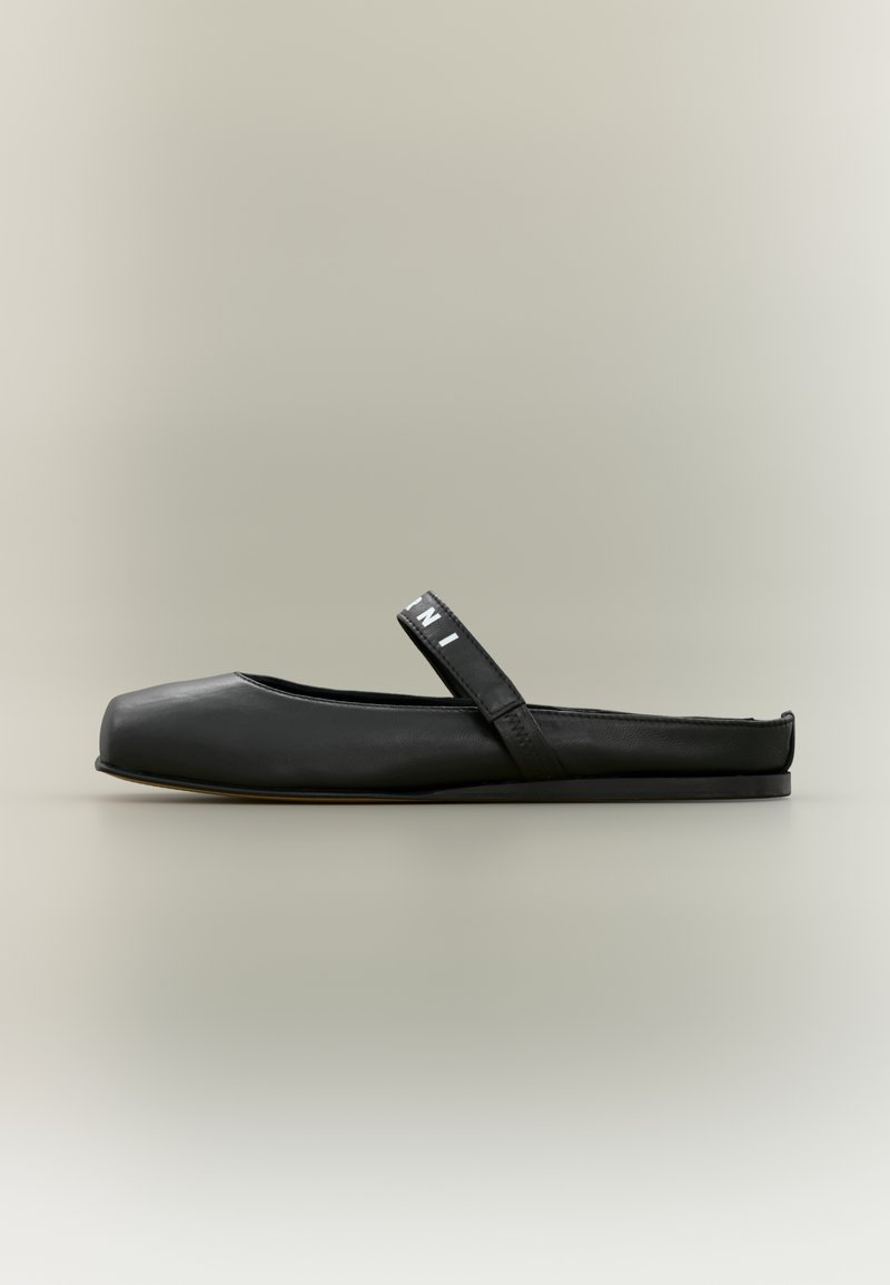 Chaussure plate noire en cuir lisse, présentant un bout rectangulaire, un talon courbé et une sangle distincte sur le dessus avec des accents de logo.