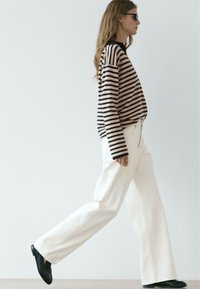 Maglione a maniche lunghe a righe beige e blu navy, abbinato a pantaloni bianchi larghi e scarpe nere, che presenta una vestibilità comoda e una silhouette moderna.